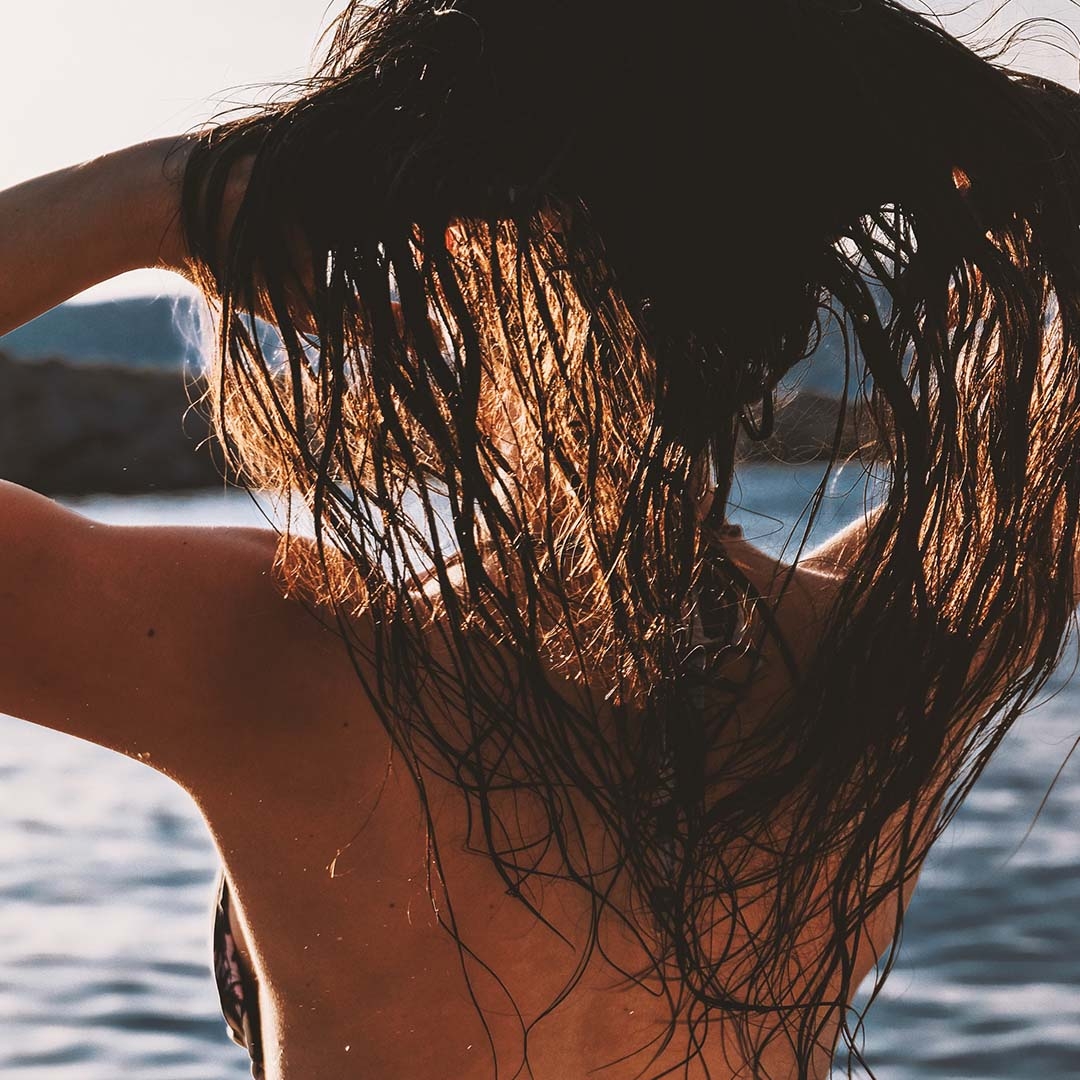 Kvinde med løst vådt hår plejet og beskyttet med Derma Supreme Leavein UV Hair Protection og Treatment kigger ud over vandet_kvadratisk